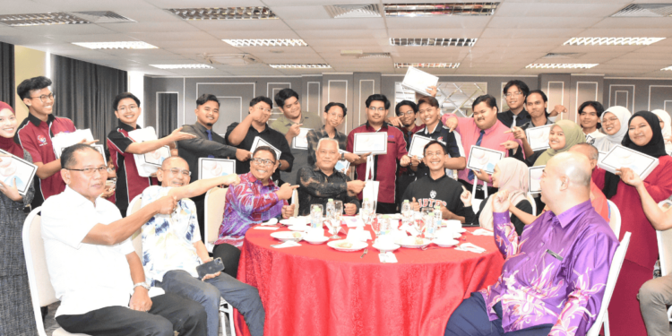 20 pelajar memegang tablet bergambar bersama delegasi MBPG serta barisan tertinggi UPSI dalam satu majlis yang diadakan di Fakulti Pembangunan Manusia, Kampus Sultan Azlan Shah, UPSI